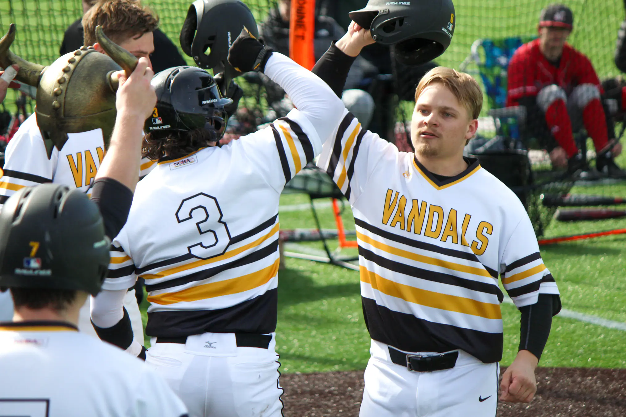 Teammates high fiving baseball helmets after a game.