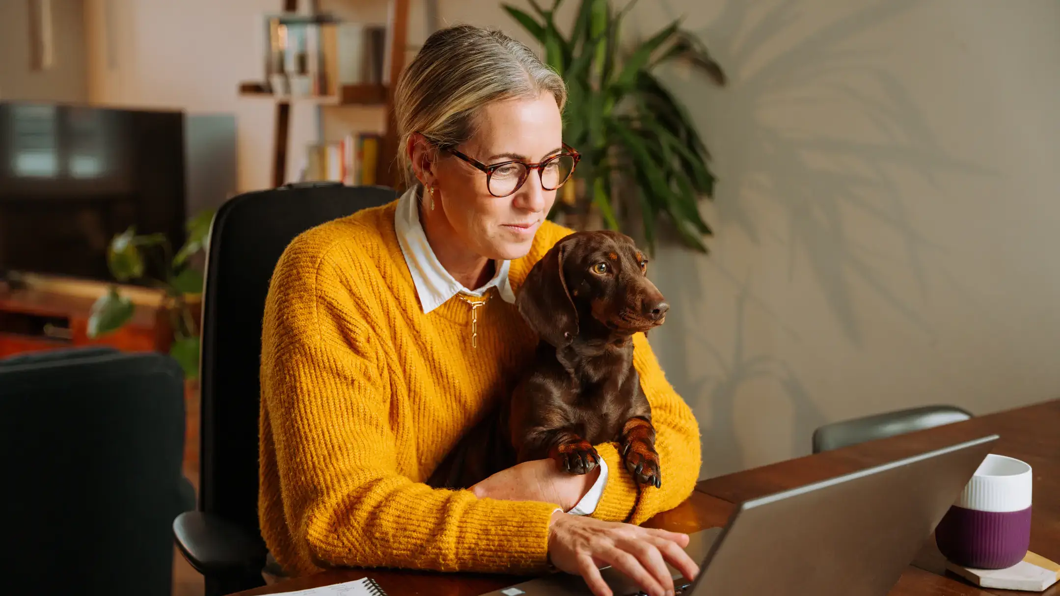 Woman studying on a laptop at home with her dog on her lap.