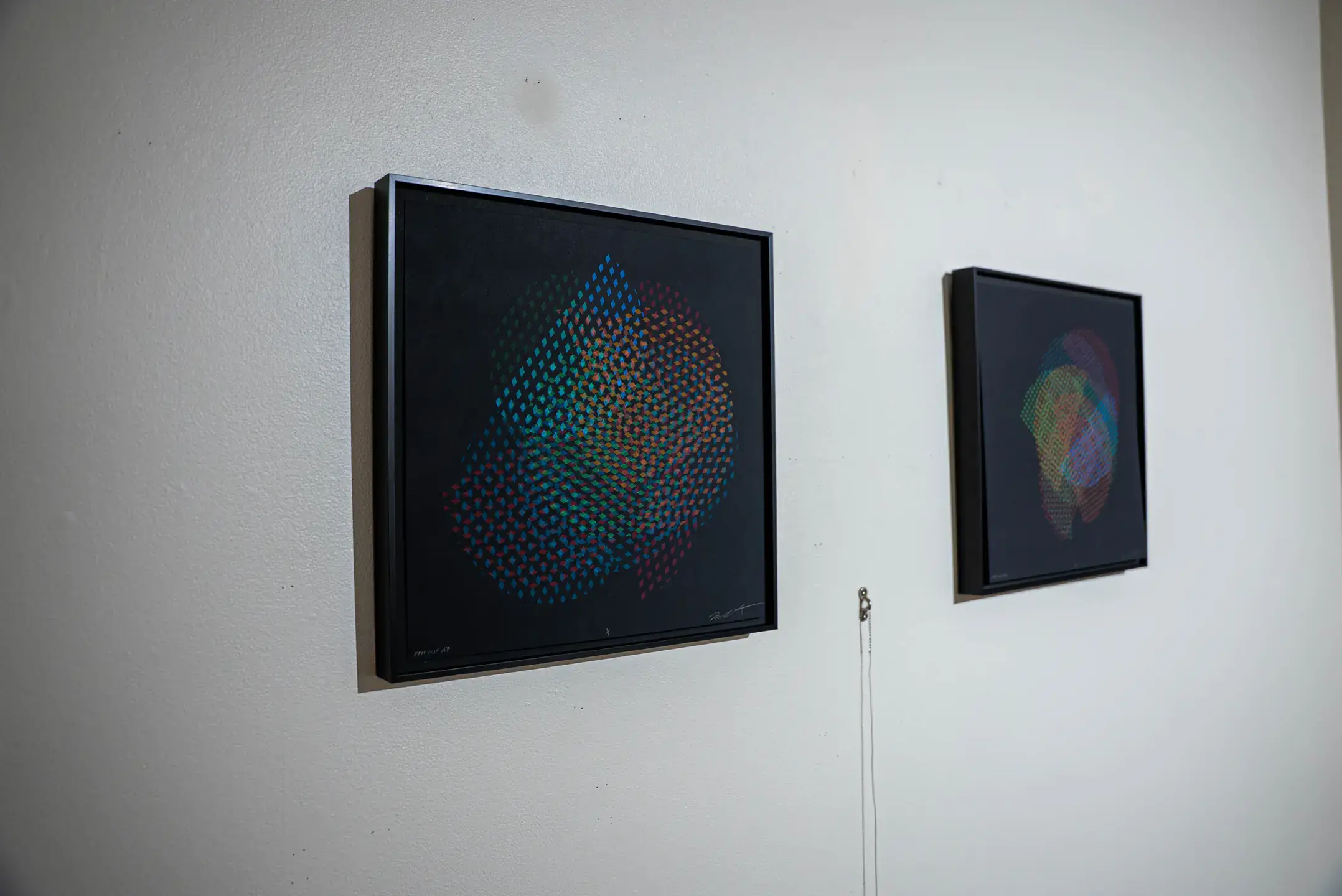 Two abstract artworks displayed on a white wall, showcasing colorful patterns within black frames.