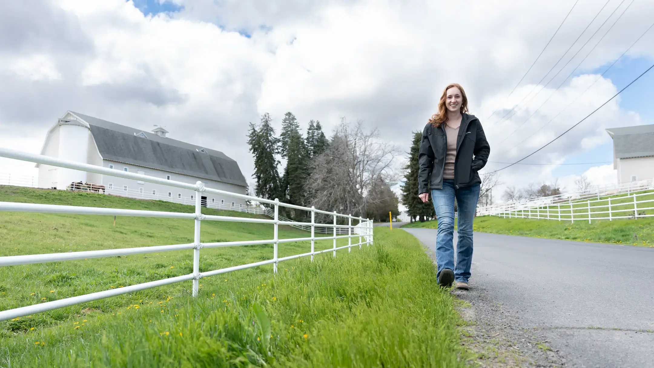 A woman walking down a road with a barn in the background.