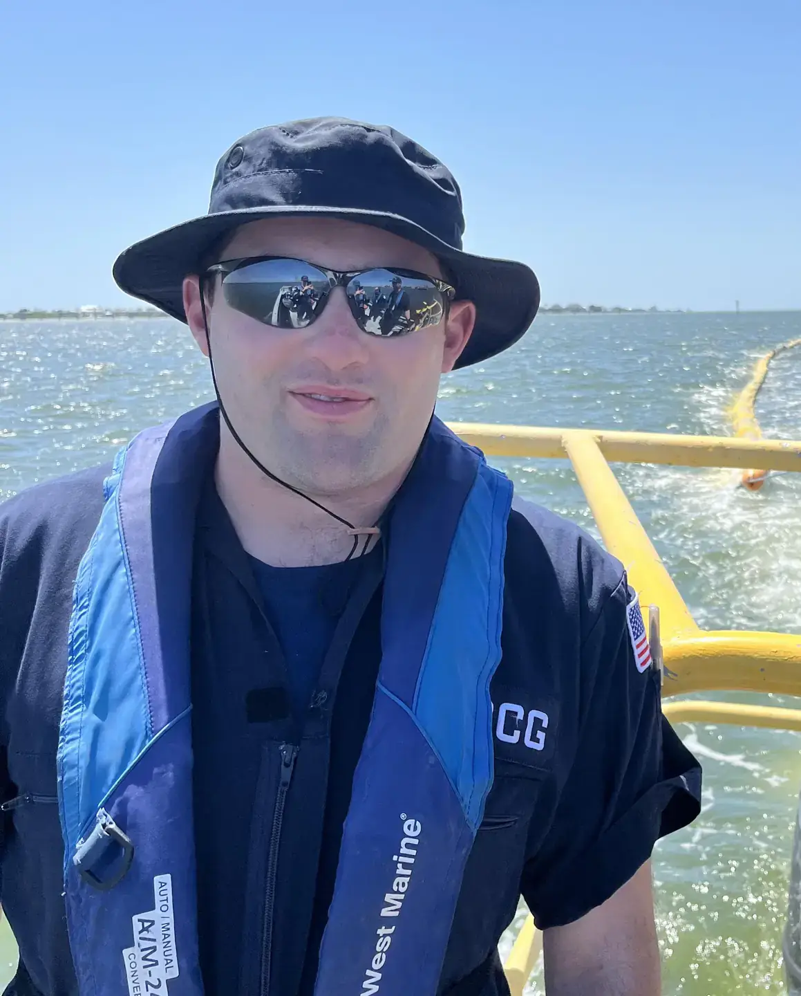 Man in boat with sun hat, shades and a life vest.