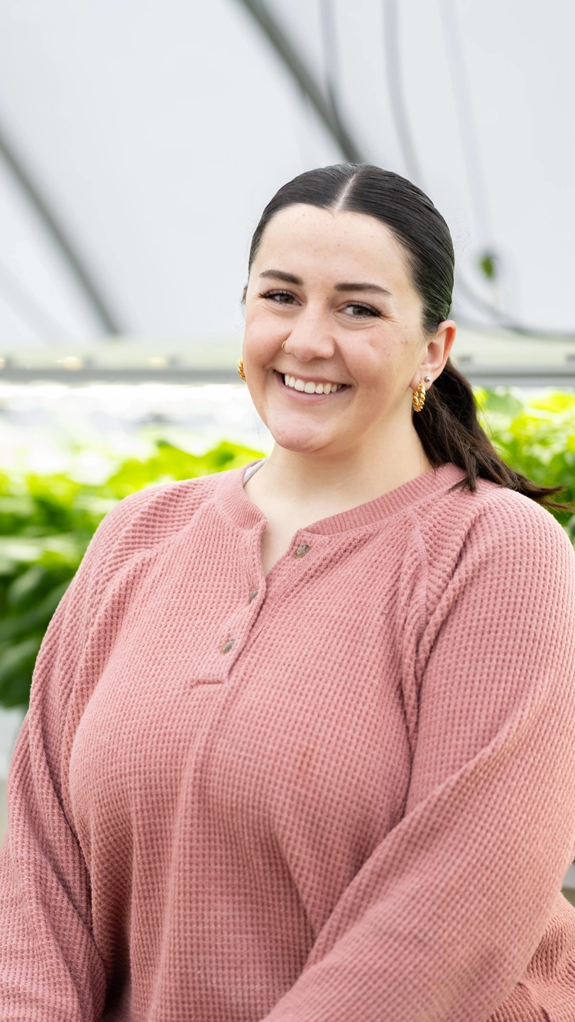 A portrait of a woman standing in a greenhouse.