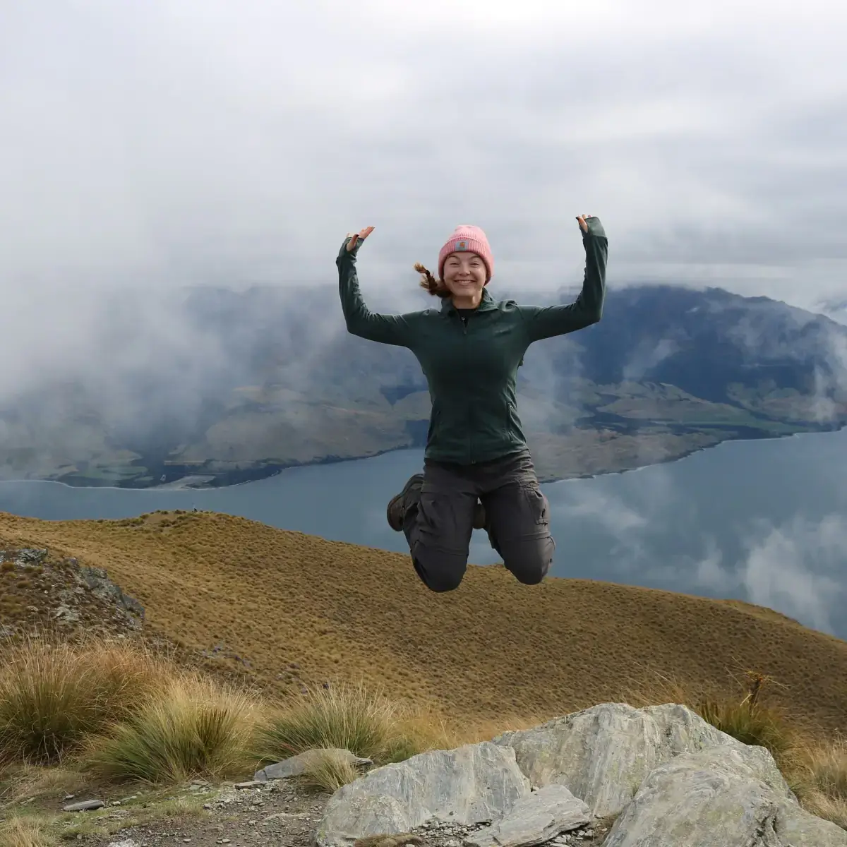 A woman jumping in the air with mountains in the background.