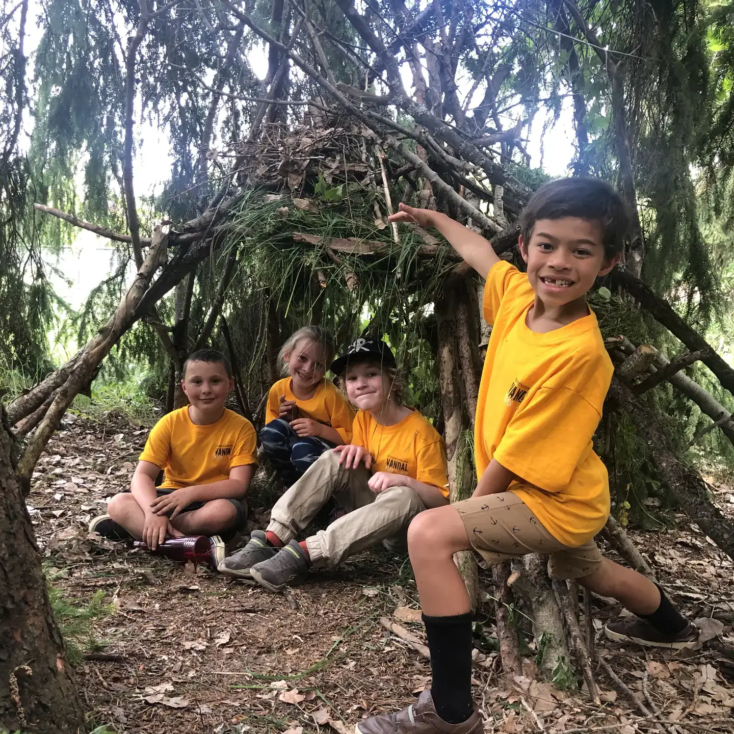 Four kids smiling in front of a wooden fort
