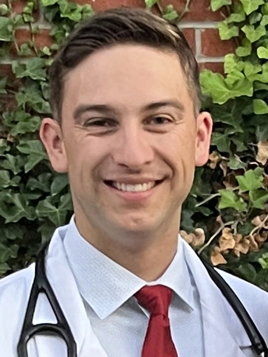 Kaden Lee smiles for a portrait outdoors while wearing a lab coat and stethoscope
