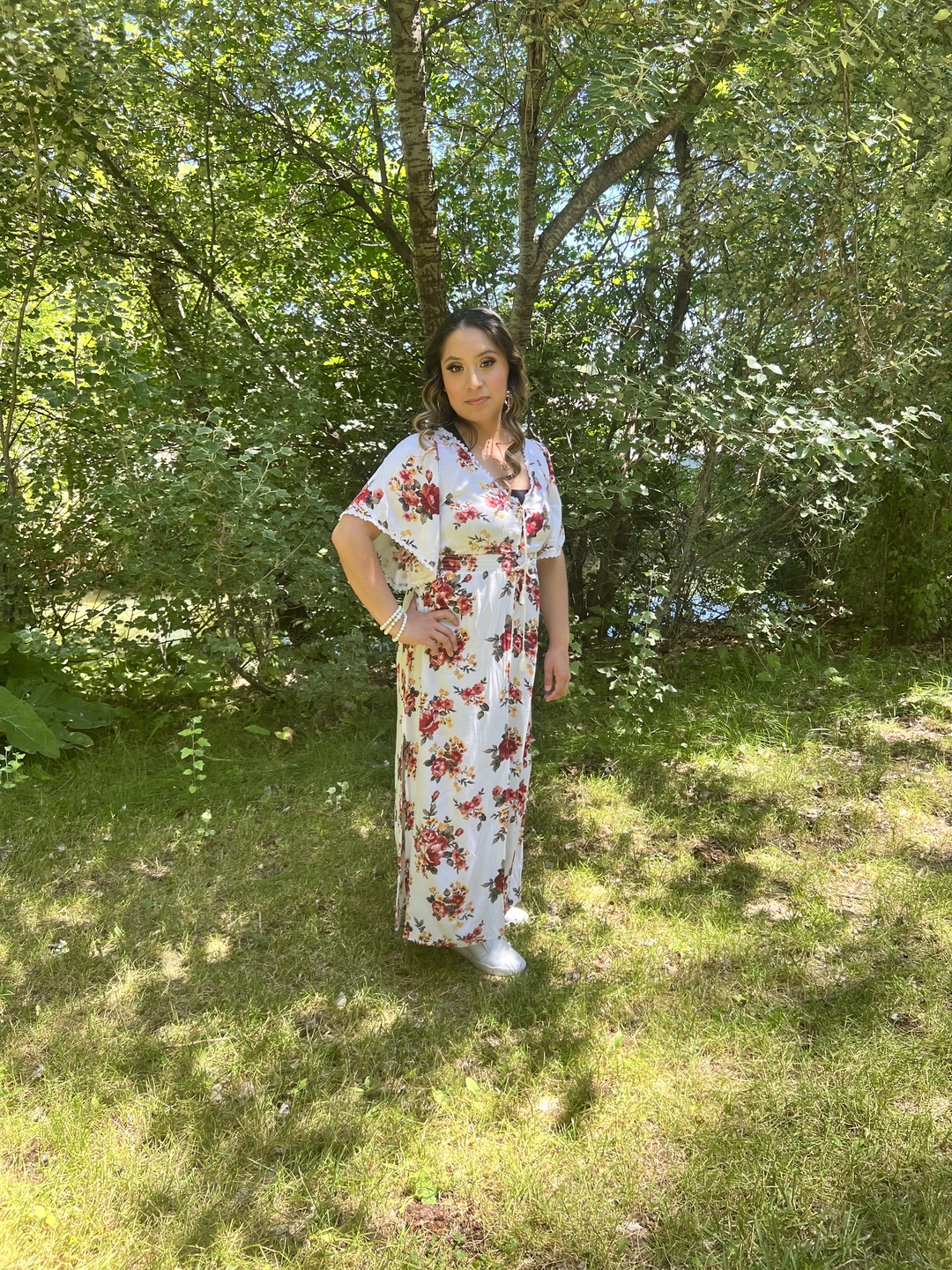 A woman in a flower dress standing in front of bushes and trees