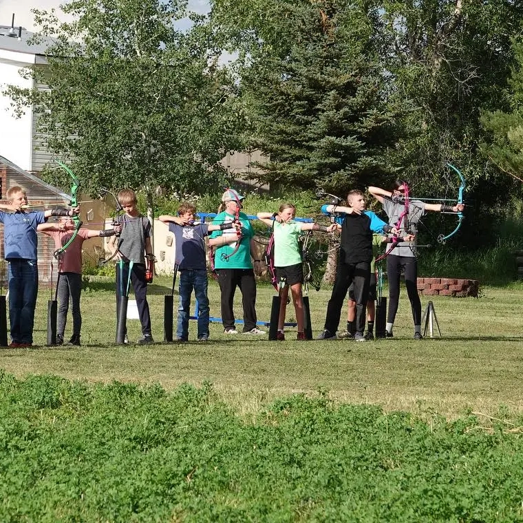 Children shoot archery under adult supervision.