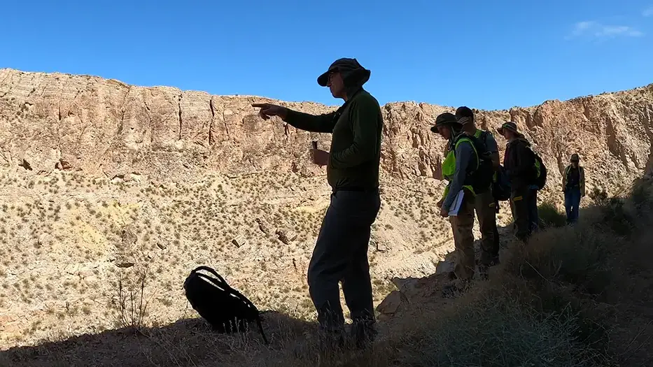 Students listen to a professor who gestures at the rocky landscape surrounding them.
