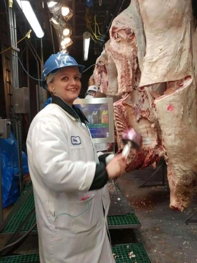 Woman in white lab coat standing next to a side of beef