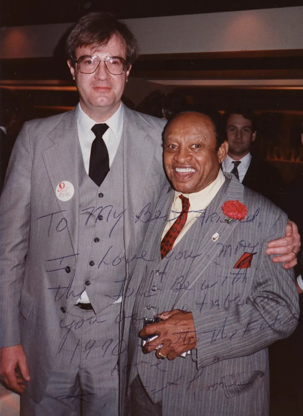 Two men in suits stand together while smiling