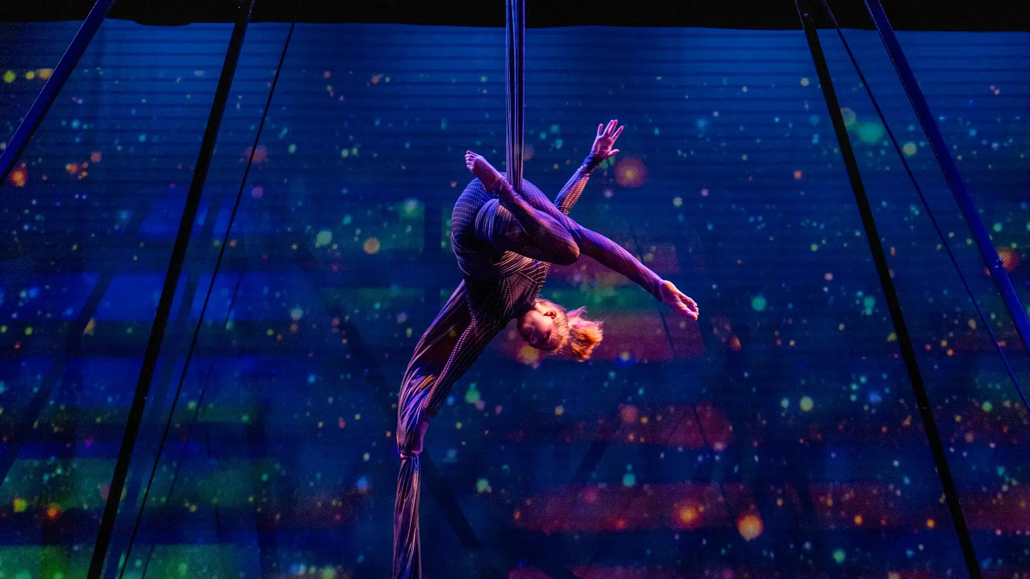  A young woman performs using an aerial sling above a lit stage.