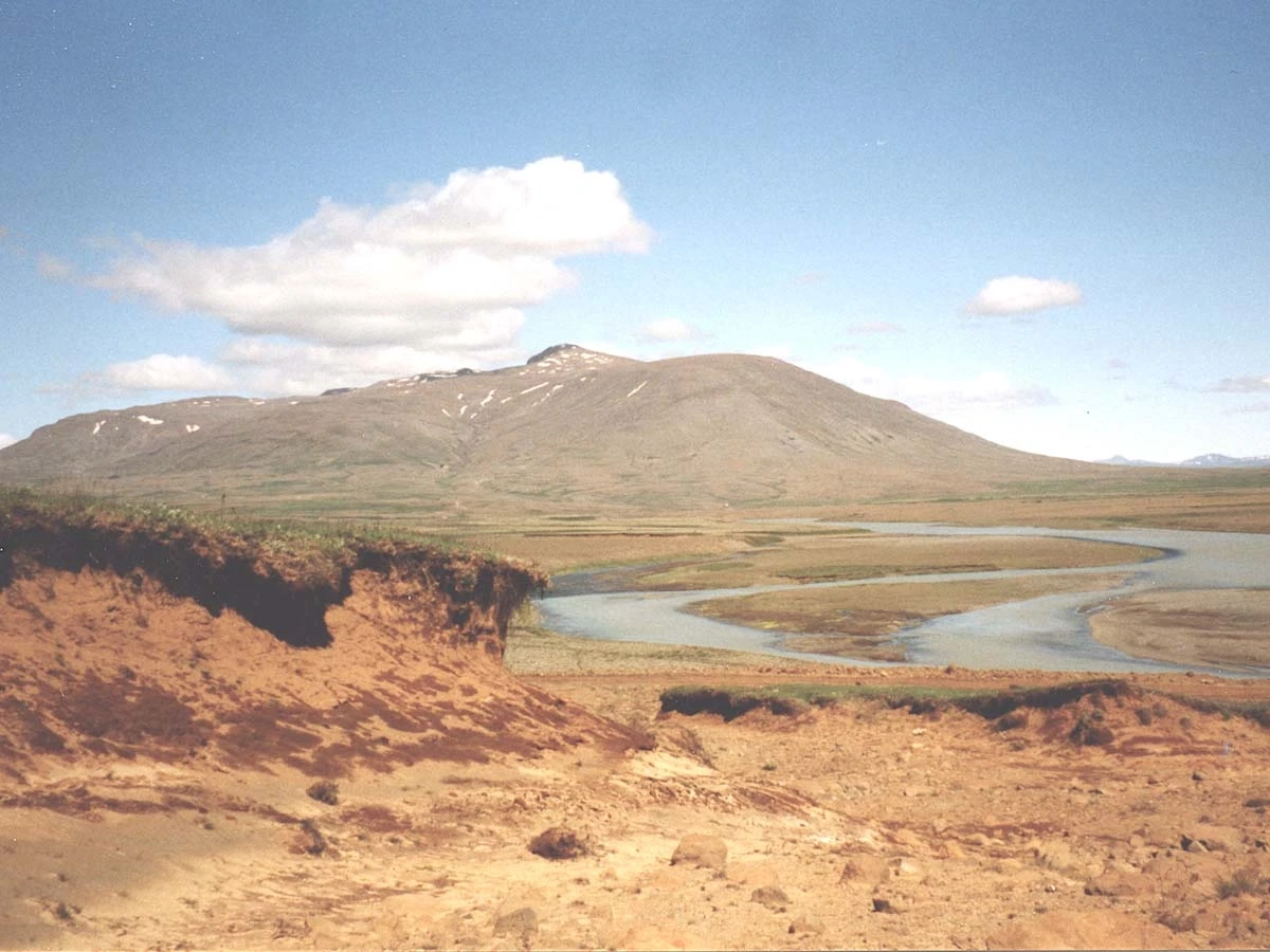 An eroded hillside of andisols includes a river and mountain in the background