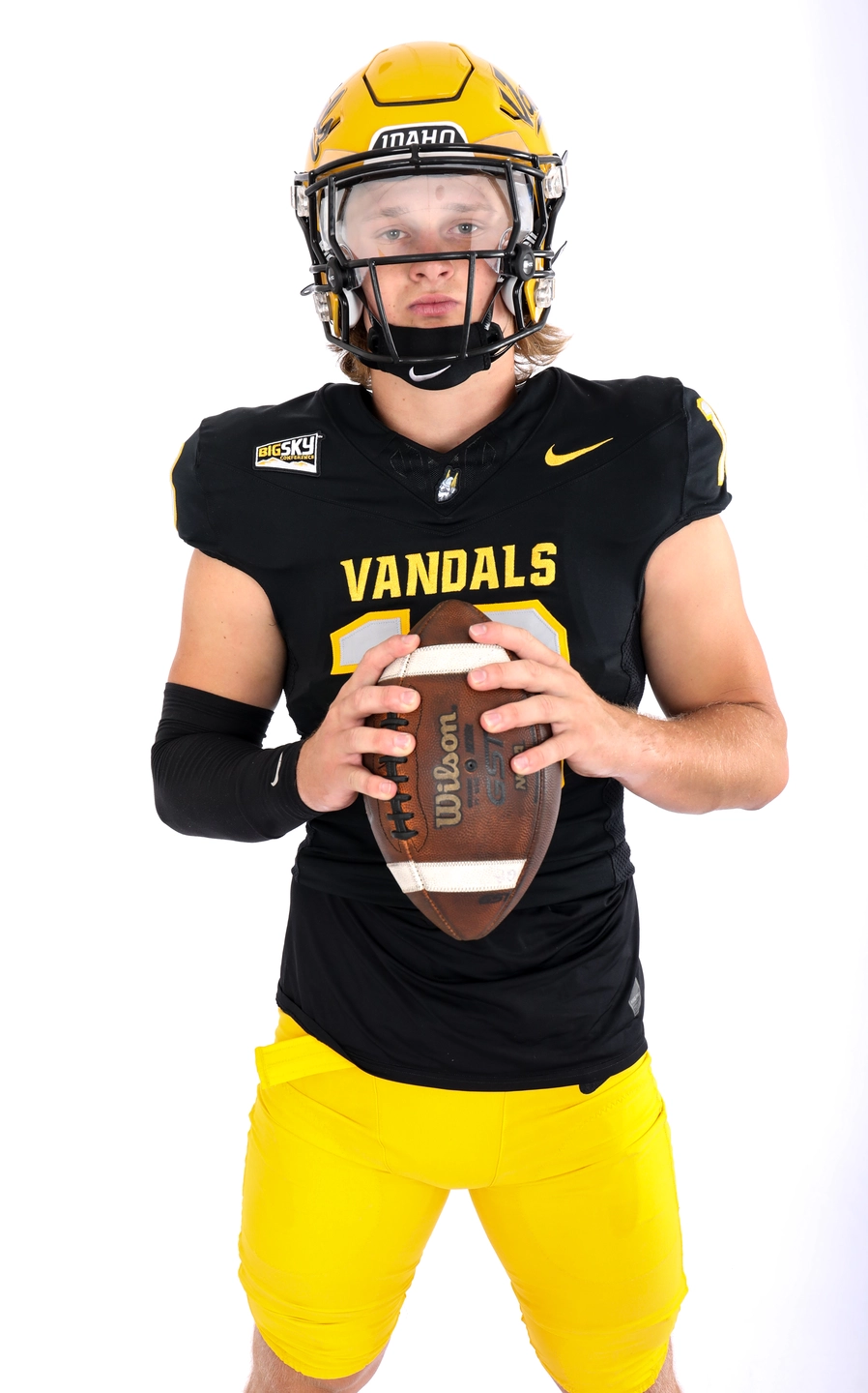 Tommy McCormick holds a football and wears gold helmet and black U of I Vandal uniform.