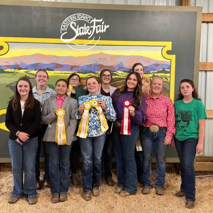 A group of children stand in front of a state fair banner holding ribbons.