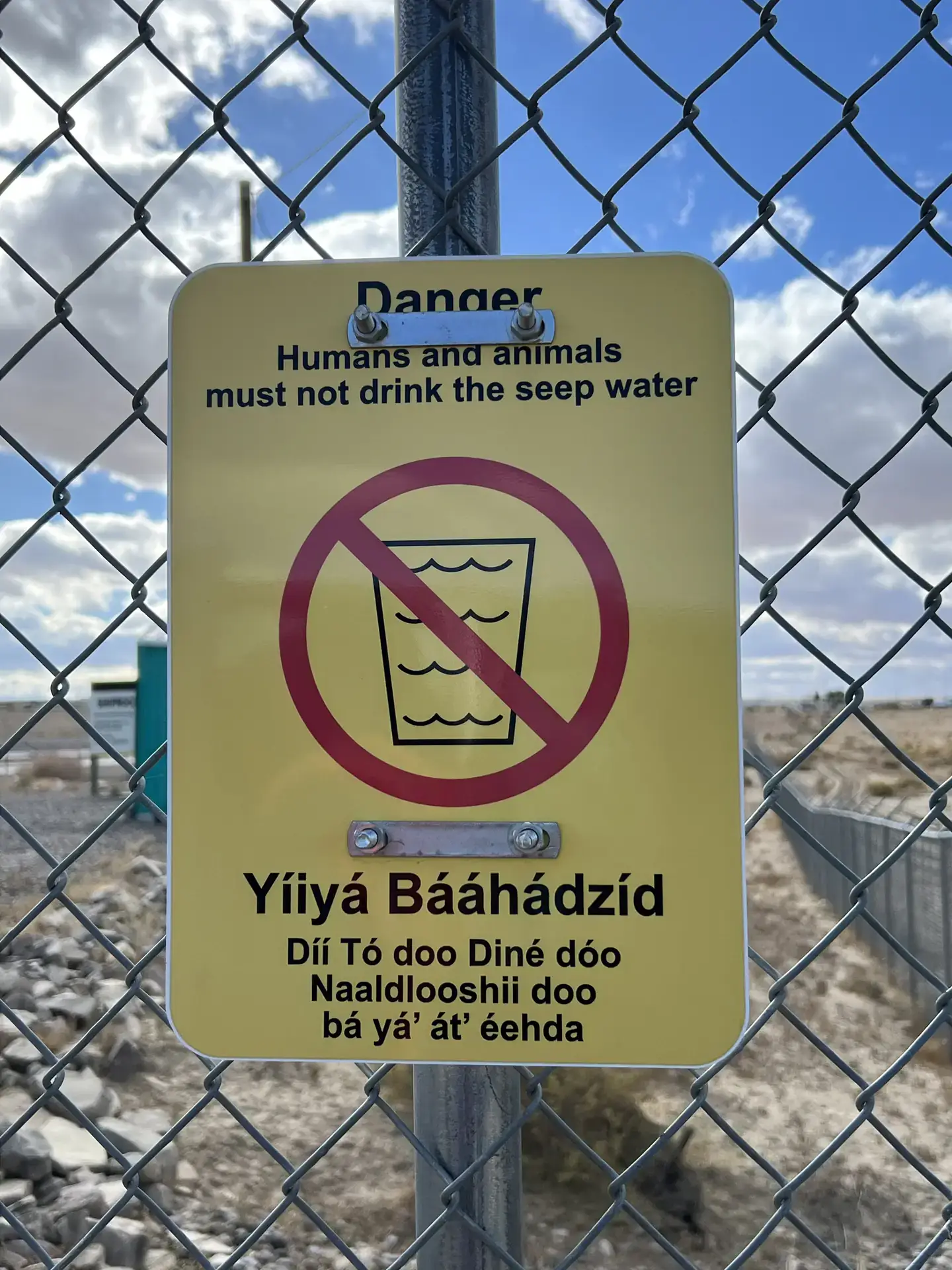 Yellow sign on fence warns seep water is unsafe to drink.
