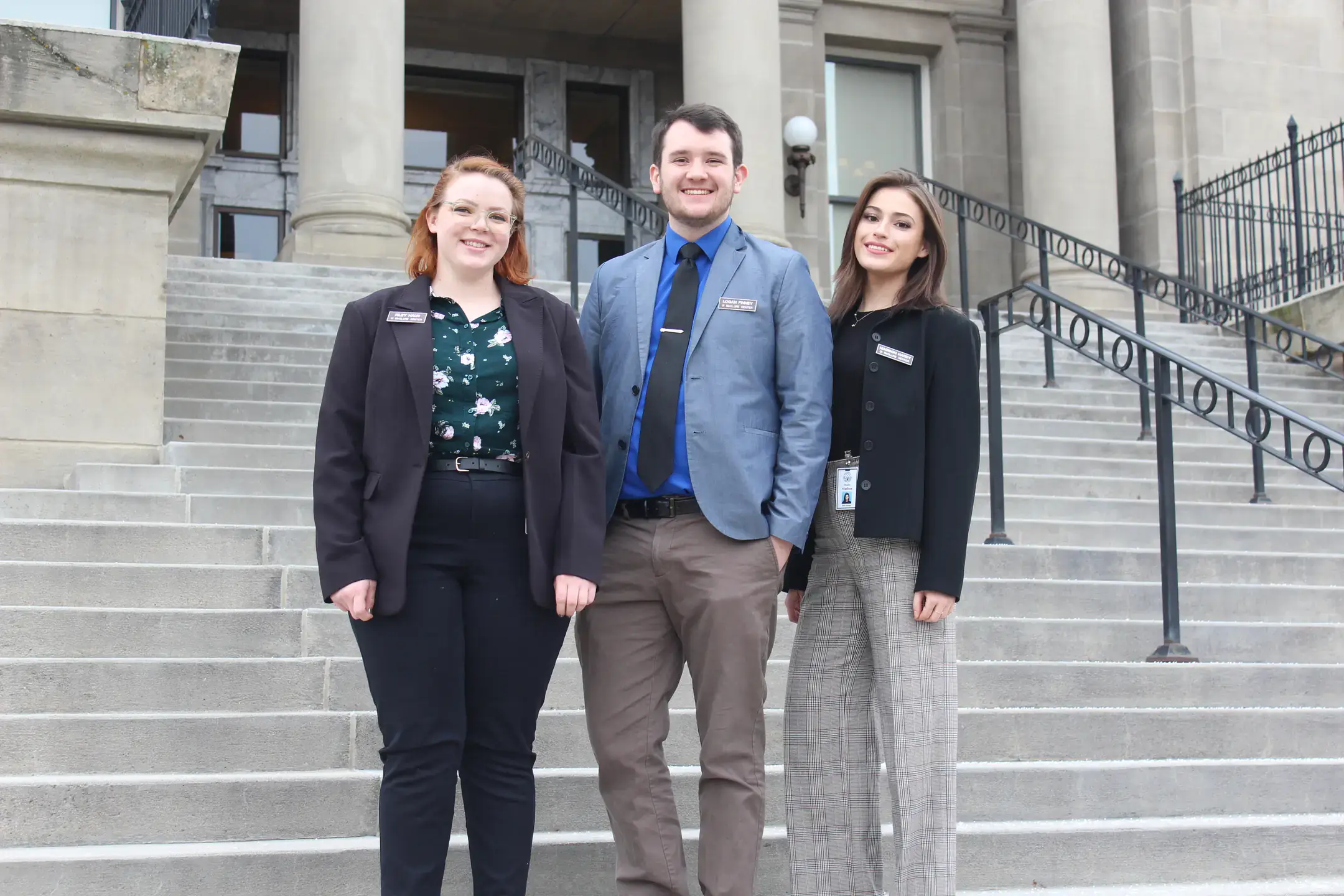 Three interns smile while standing on stairs outside a government building.