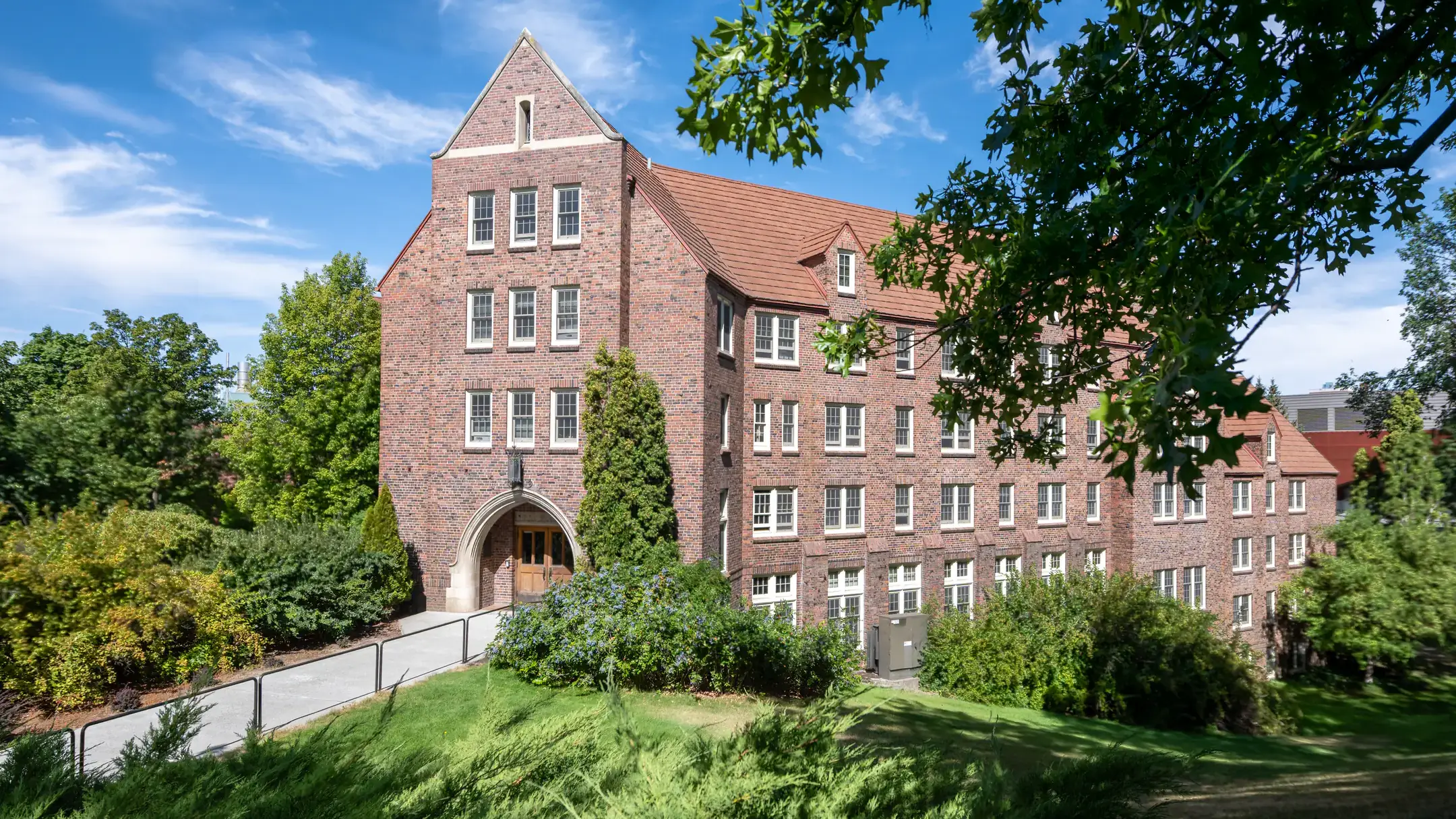 A brick building with red roof surrounded by trees and greenery on a sunny day.