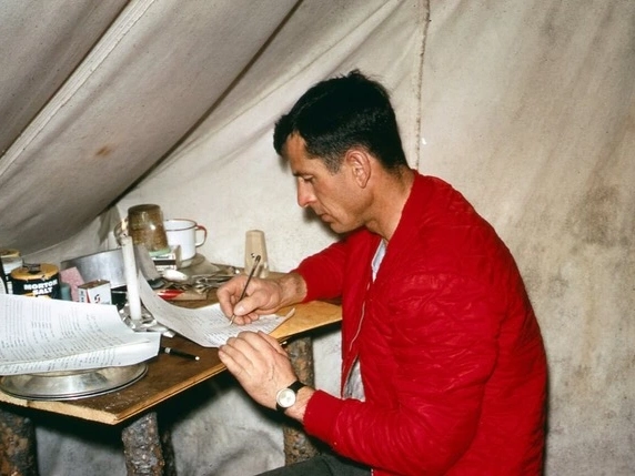 A man sits in a tent and writes in a notebook
