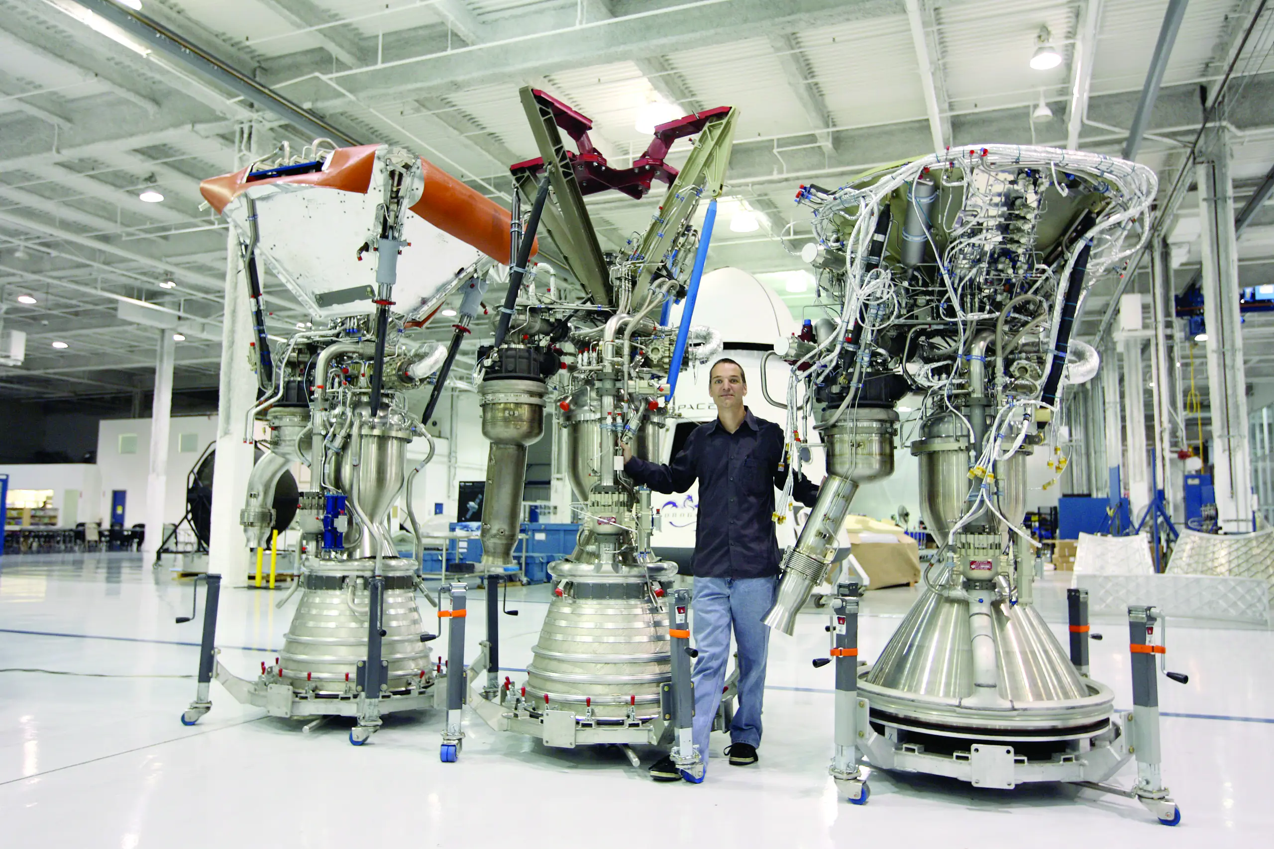 Tom Mueller poses with three SpaceX rocket engines, which are twice his size.