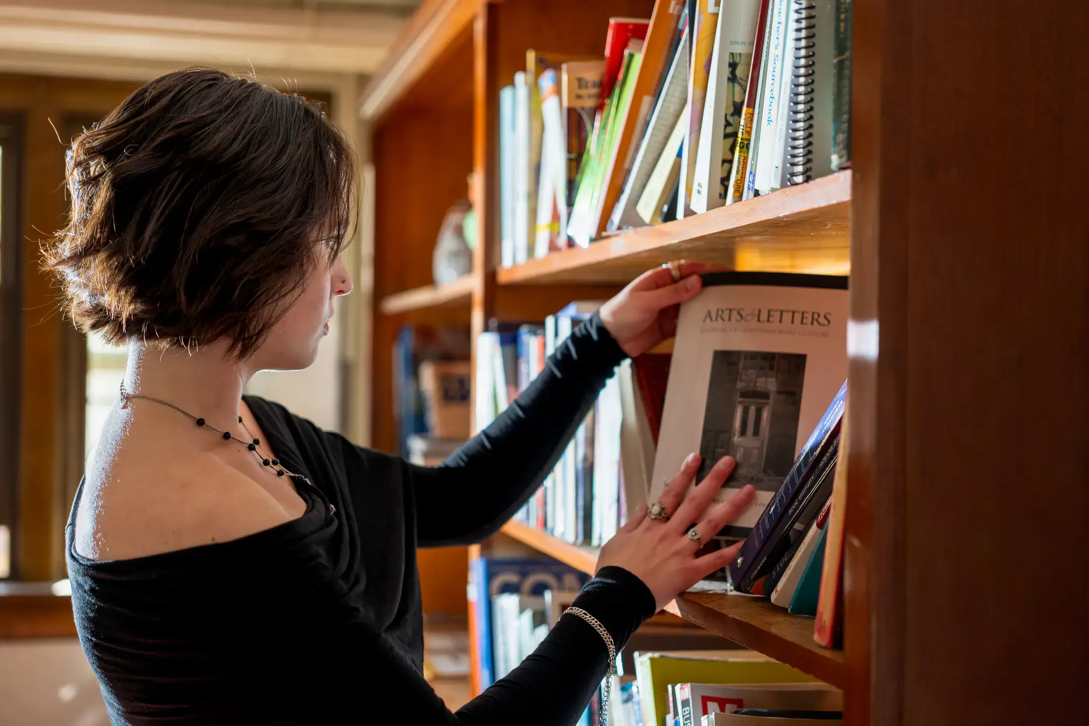 Person selecting a book from a wooden library shelf in warm sunlight