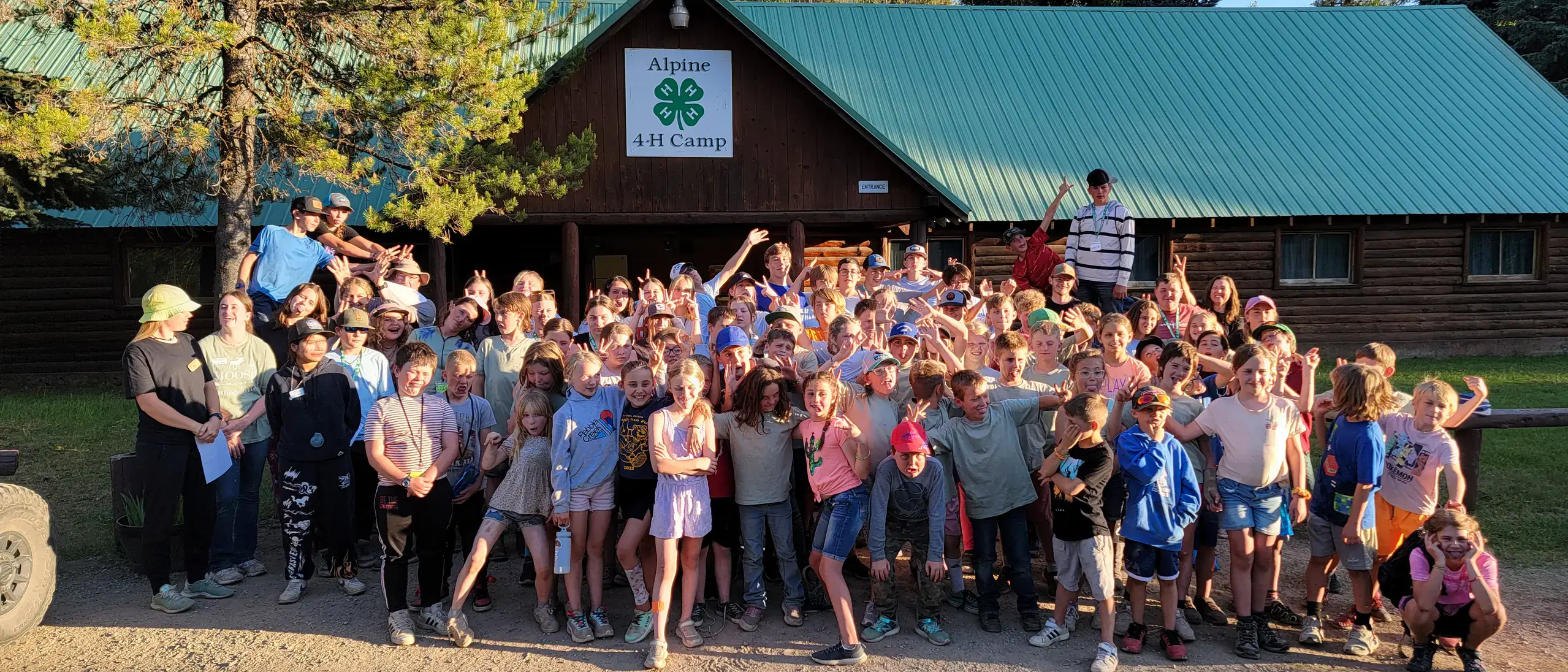 group poses outside cabin with 4-H clover