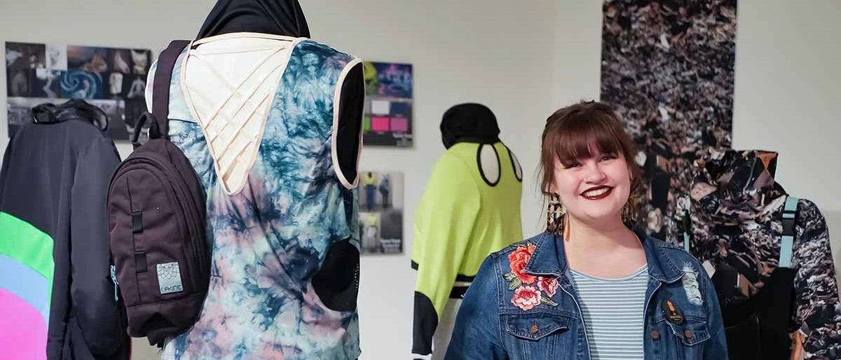 U of I student standing in a gallery showcasing her clothing designs. 