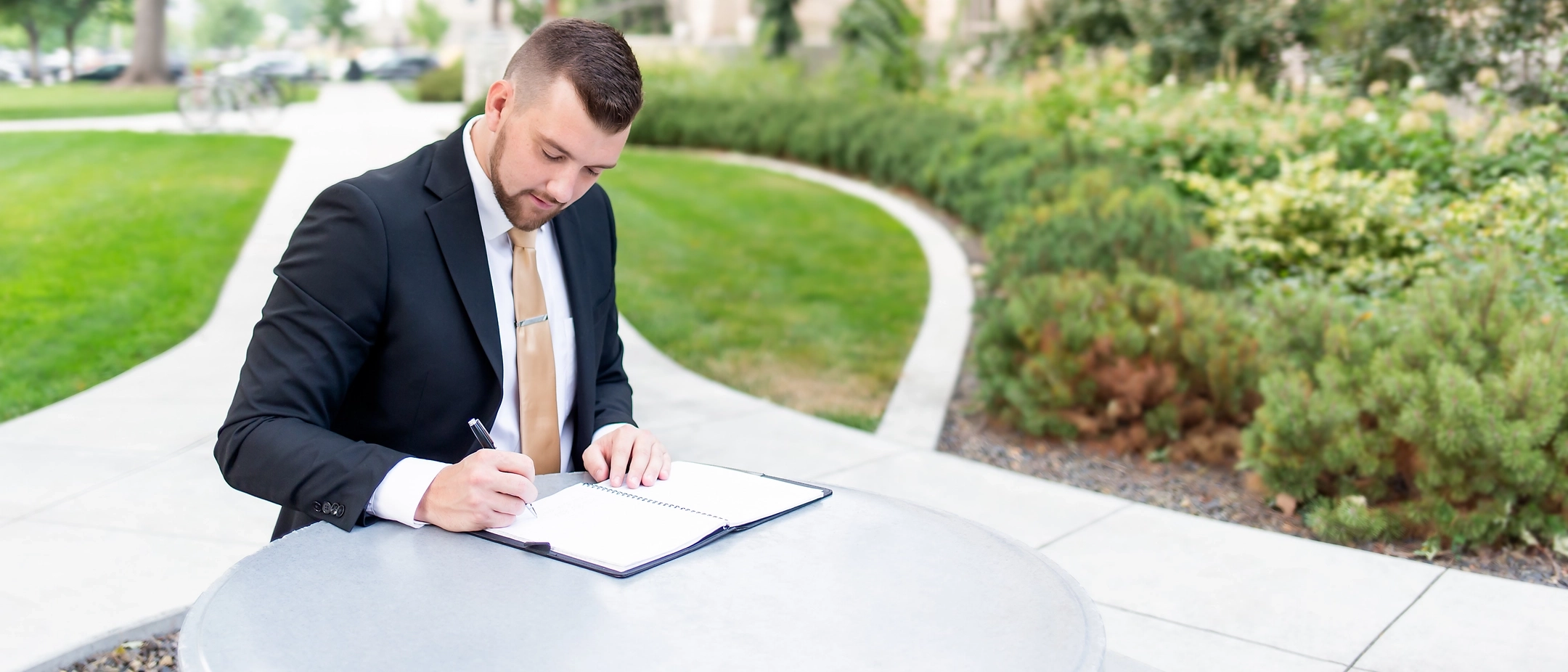 Student in business attire sitting down writing outside