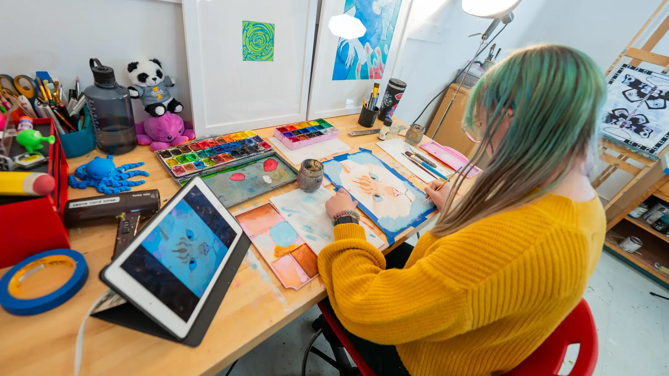 Kieran Heywood wearing yellow shirt painting a cat at their desk. 