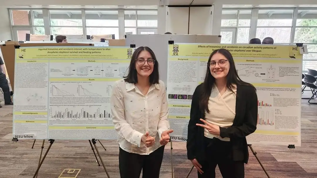Two women wearing glasses stand in front of science posters