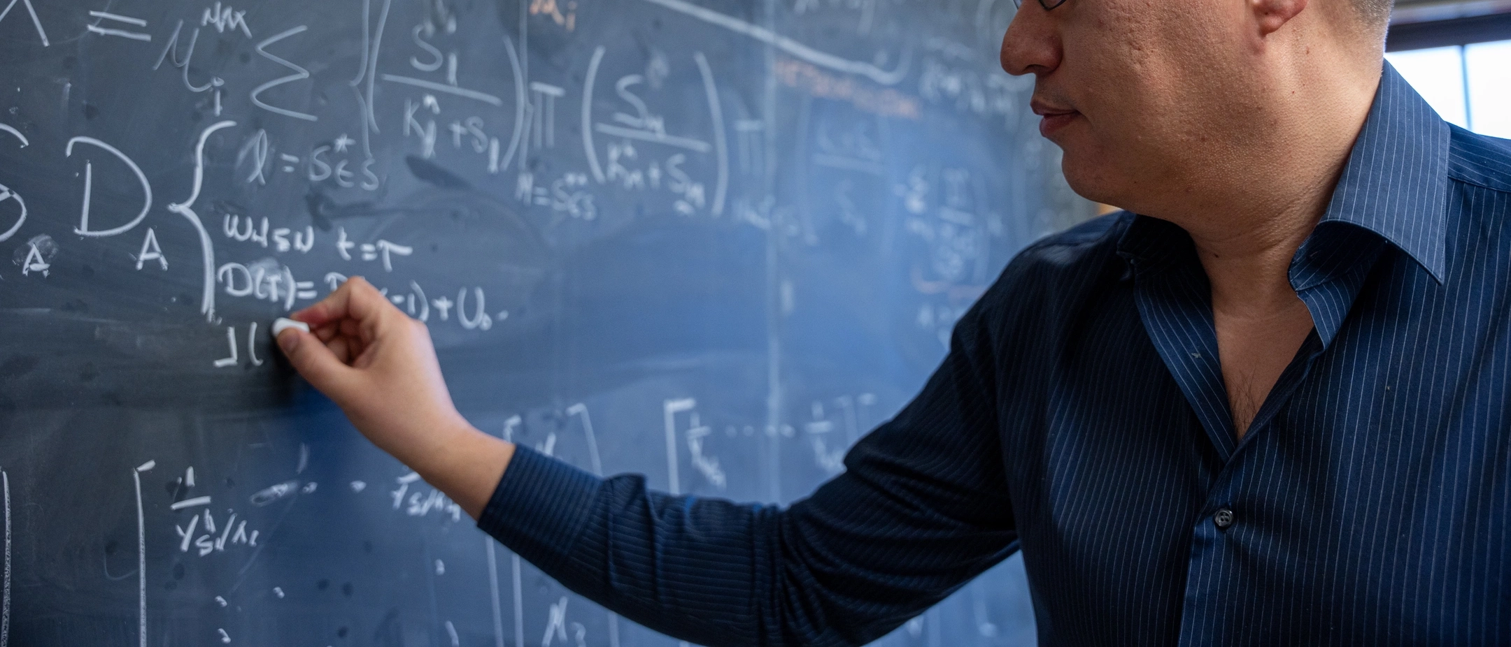 Assistant Professor of Mathematics, Esteban Hernandez-Vargasriting, presenting math equations model on a chalkboard to study the mitigation of viral infections.
