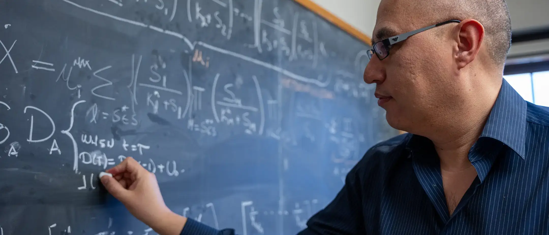Assistant Professor of Mathematics, Esteban Hernandez-Vargasriting, presenting math equations model on a chalkboard to study the mitigation of viral infections.