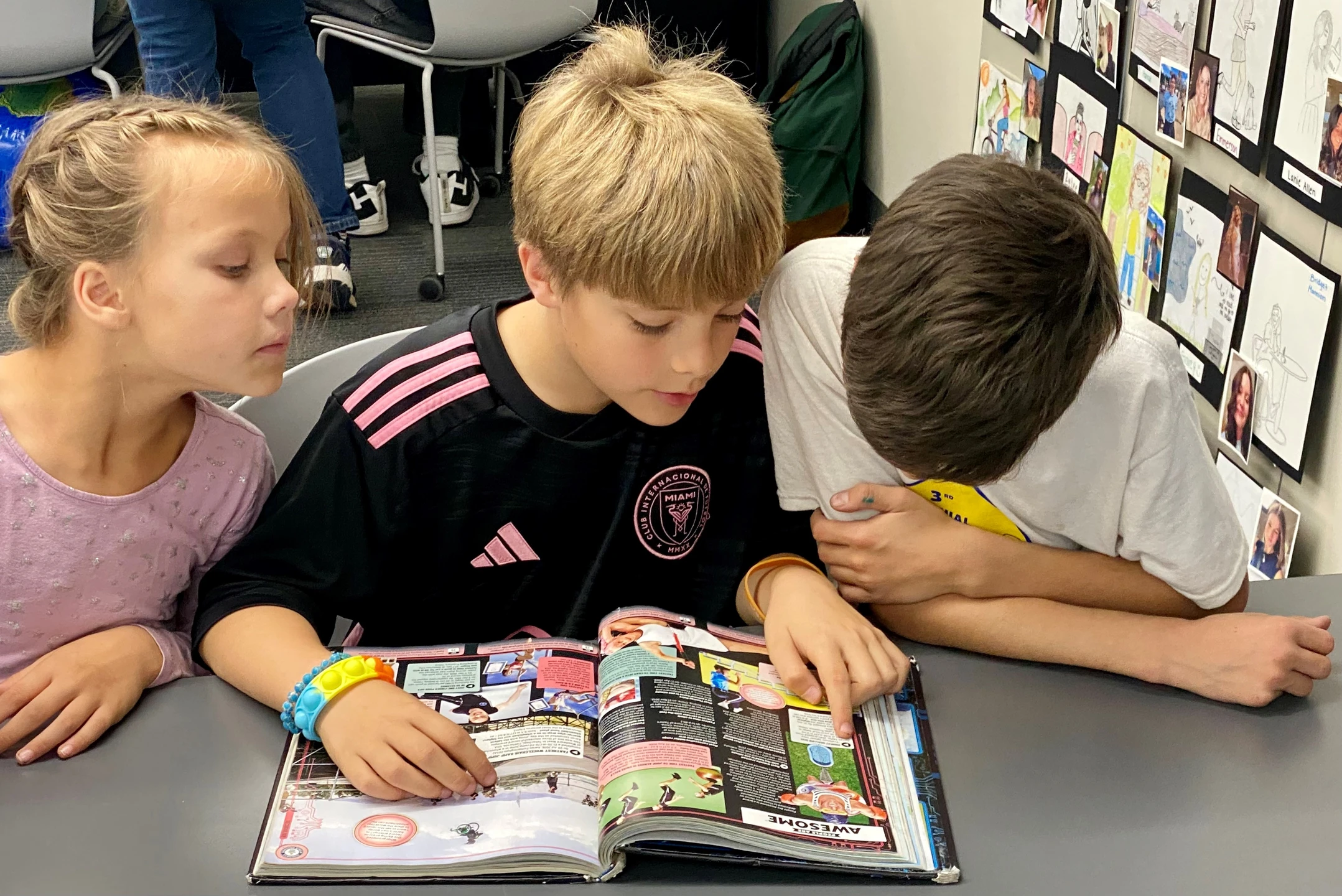 Photo of two boys and one girl reading the same book.