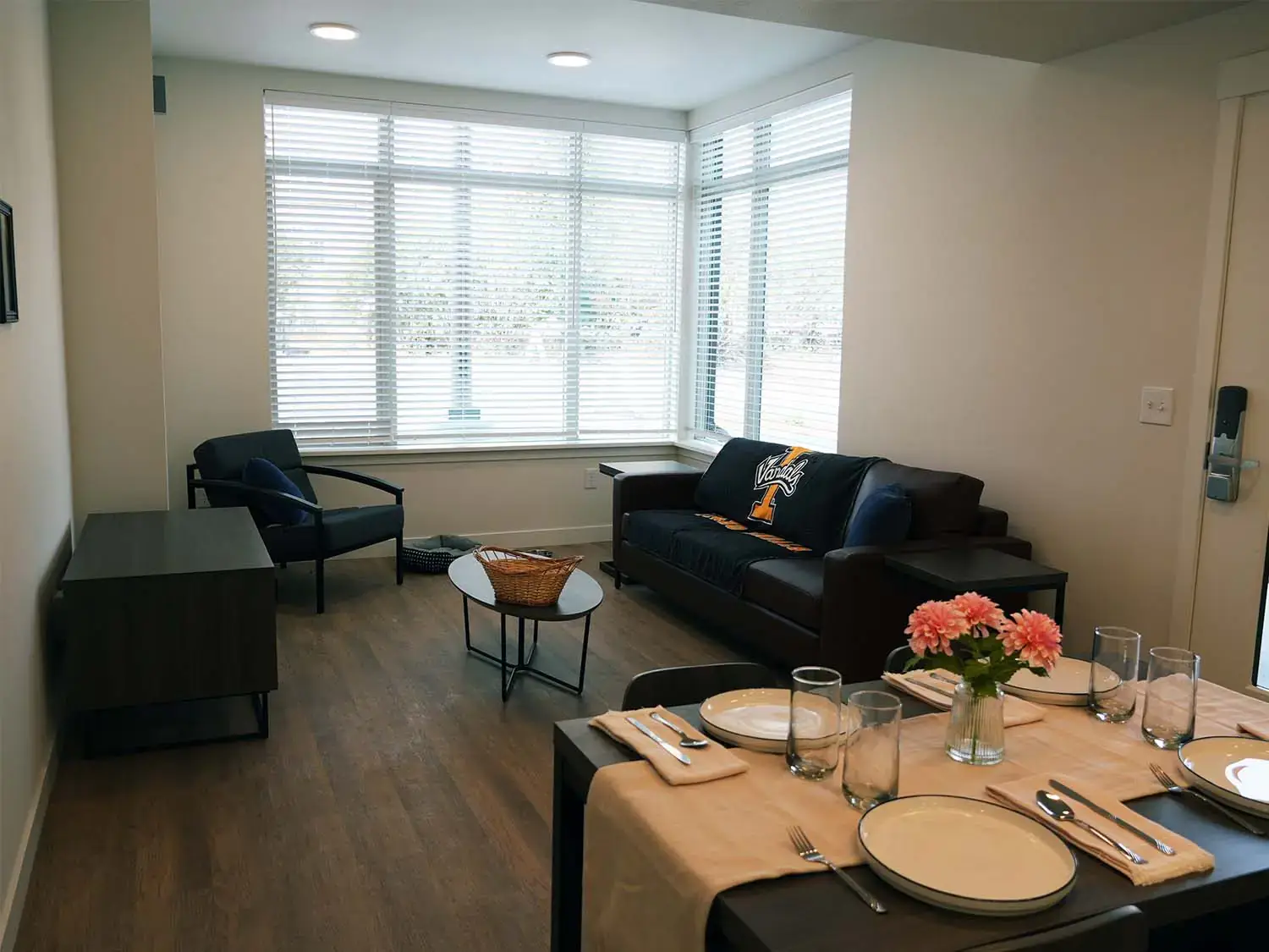 Living room and dining area in a Vandal Village Family Housing apartment with large corner windows, comfortable seating, and natural light.
