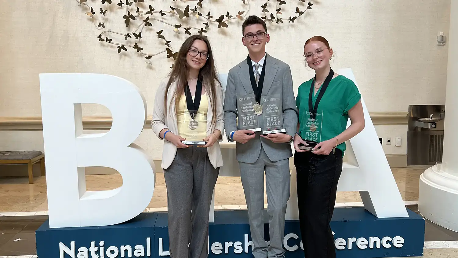 U of I BPA chapter members Rylee Wimer, Colton Moore and Sophia Gill stand in front of a BPA sign and hold their awards. 
