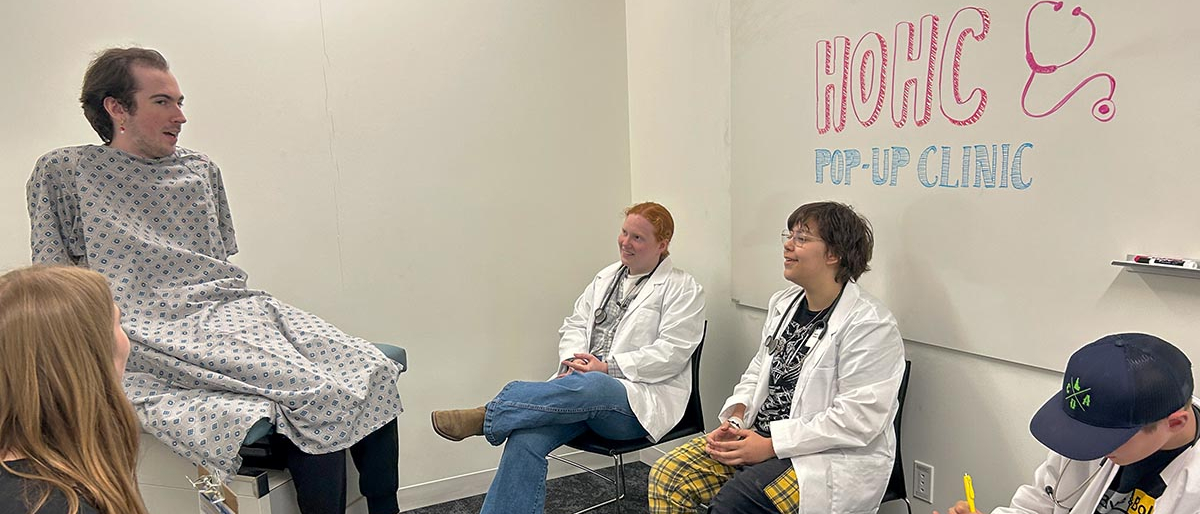 Three students wear white coats pretending to be doctors.