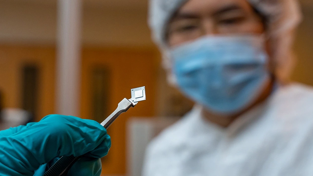 Student in lab wearing protective gear holding a microchip with tweezers.