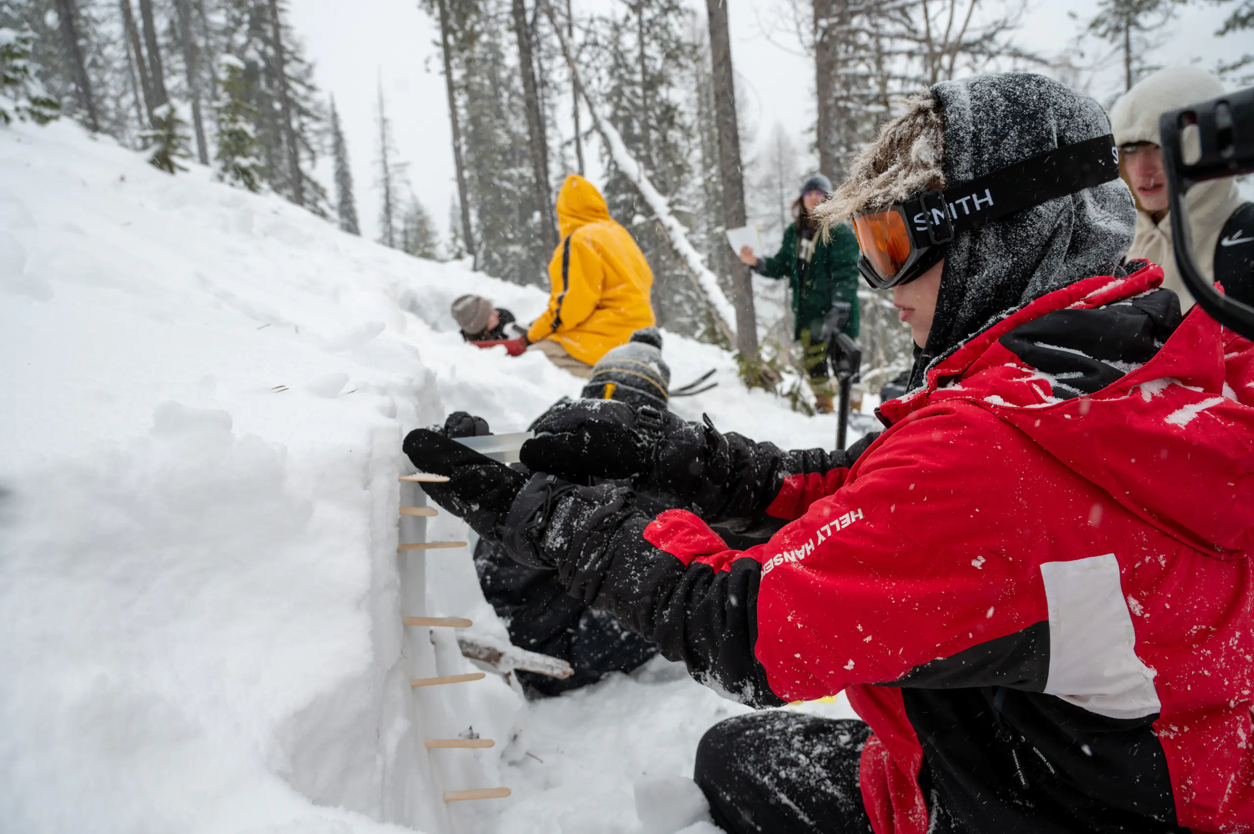 A student takes a snow sample for snow-water equivalency in a snow pit
