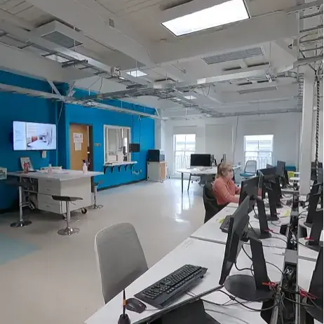Students in room with computers at desks and a blue wall in the background.