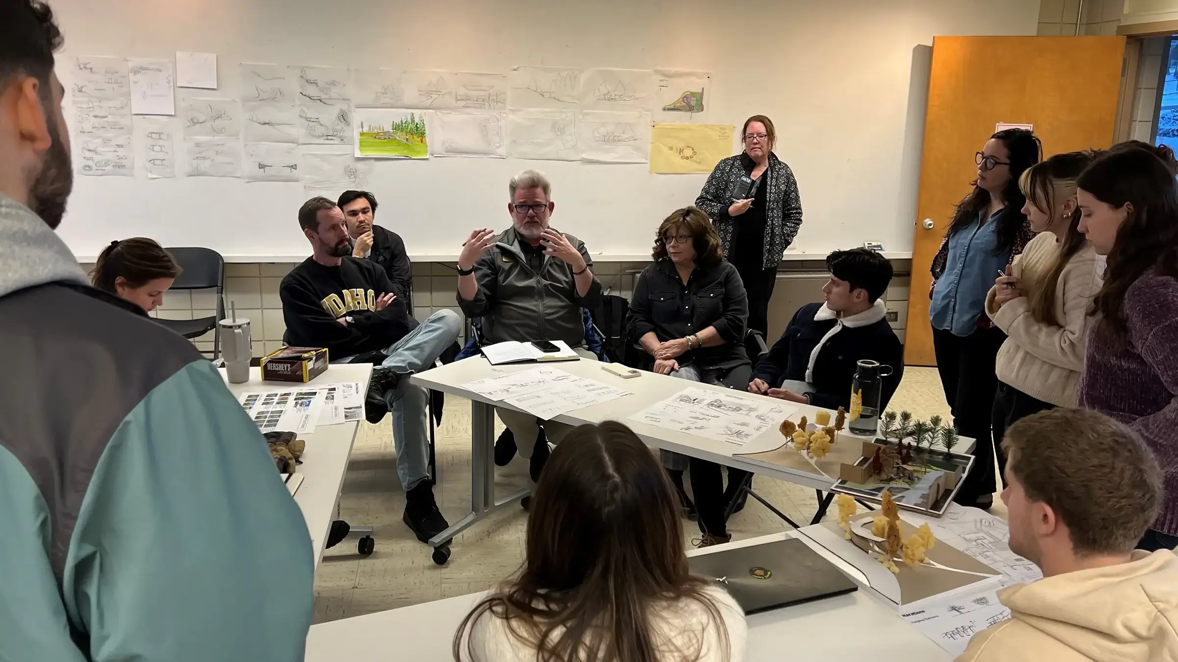 Photo of students and faculty sitting around tables with drawings in the background