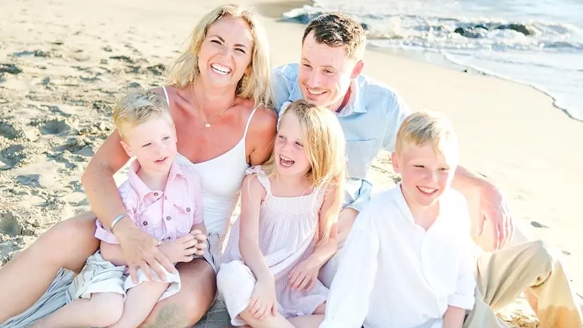 A man sits on the beach with his partner and three children.