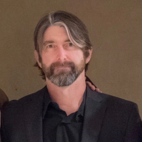 A headshot of a man smiling while wearing a black tux