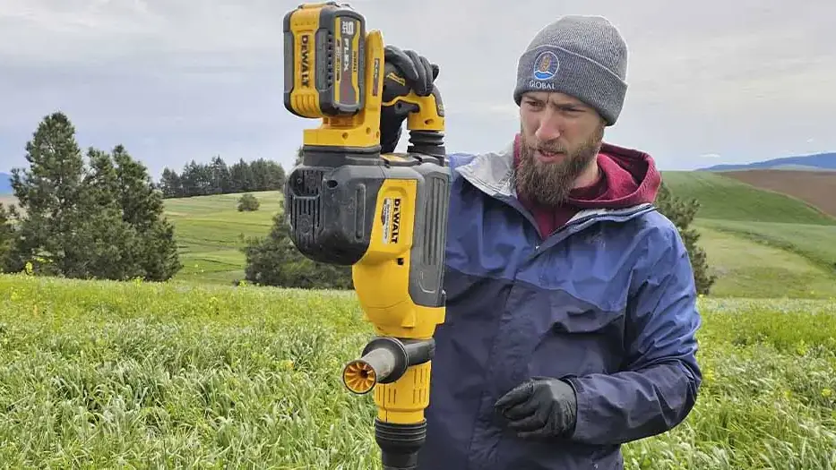A man inspects machinery outdoors while standing in rolling fields of the Palouse