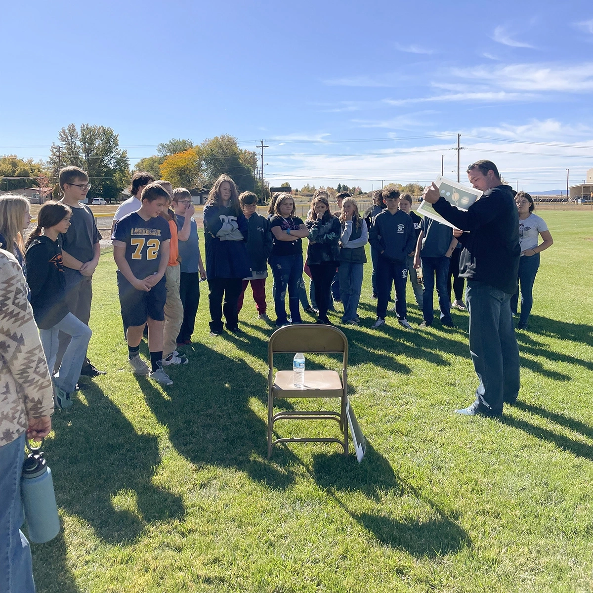 A group of students stand outside and listen to a lecture.