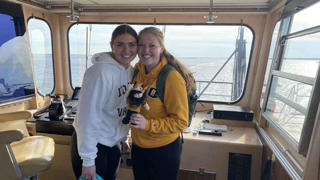 Two women smile at the camera in the deck of a boat.