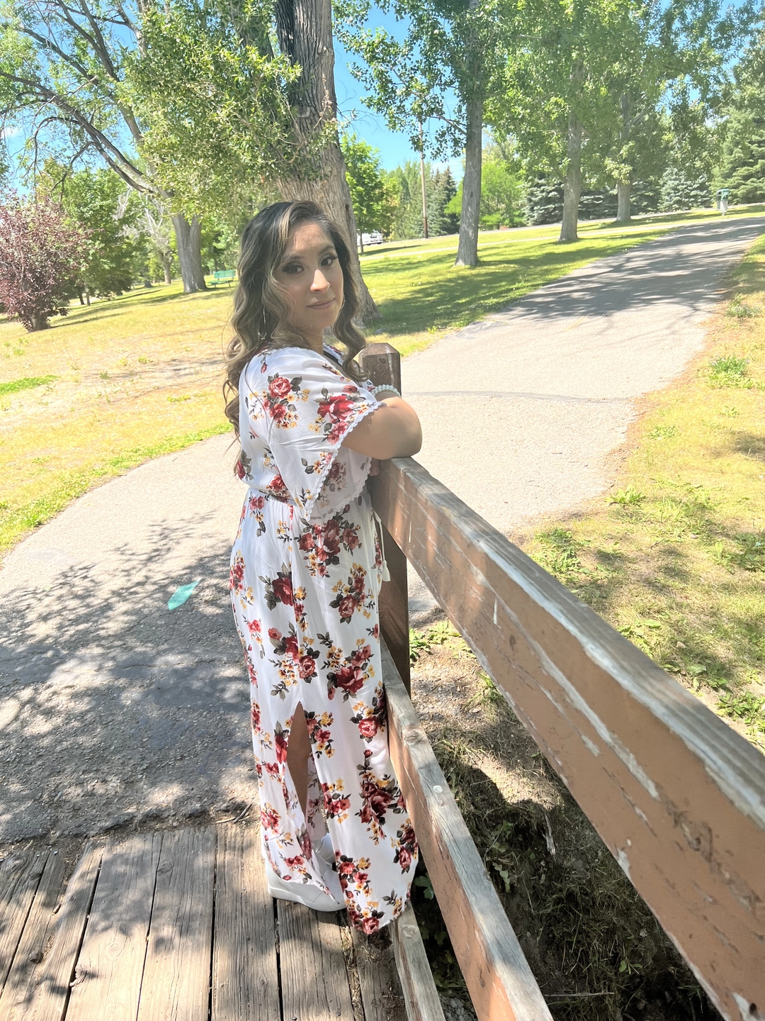 A woman in a flower dress standing in front of bushes and trees