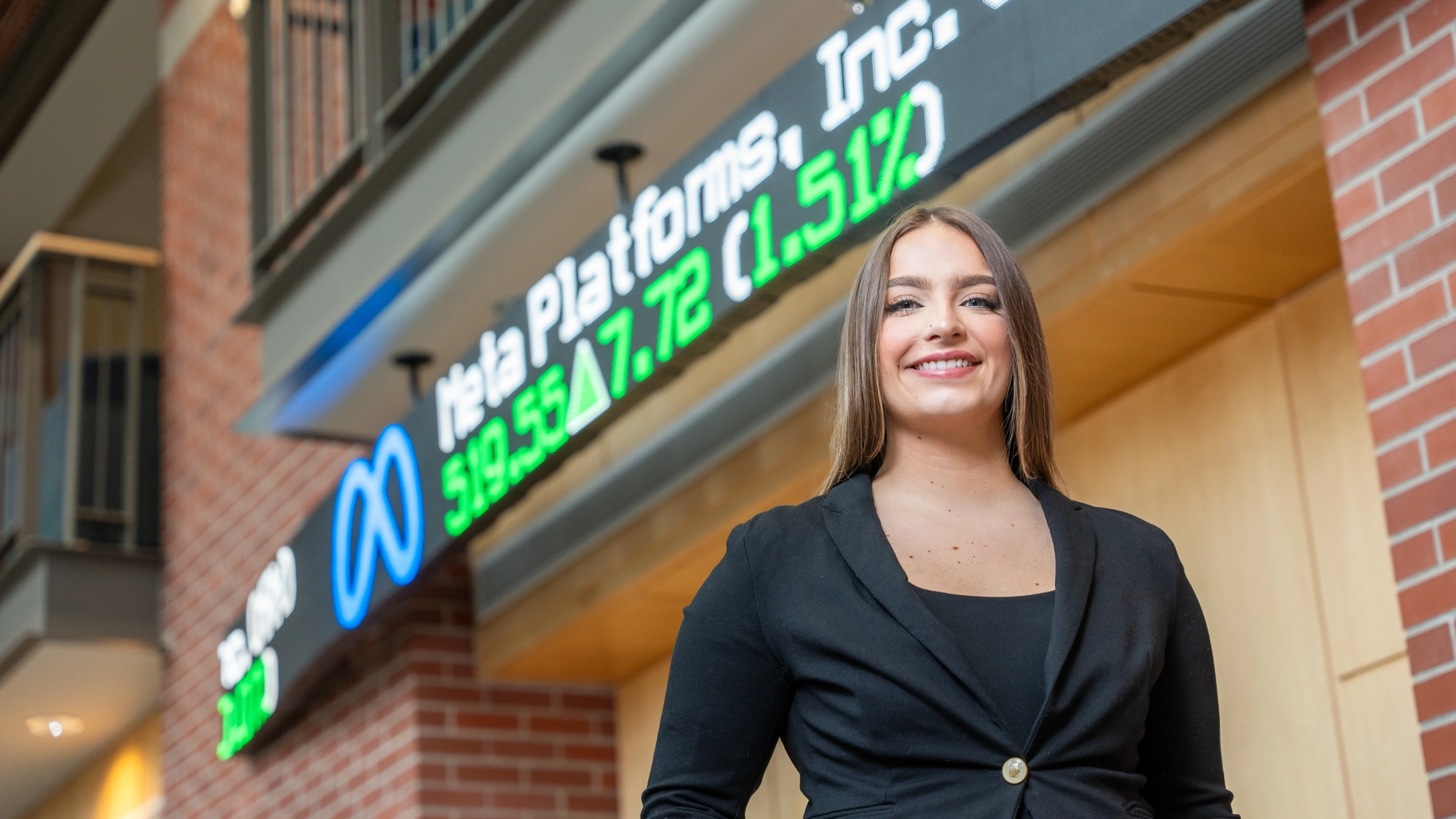 Anna Bliss stands in front of market price LED ticker display board
