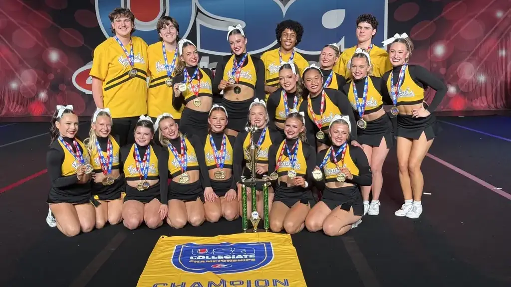Men and women wearing black and yellow Vandal uniforms posing in front of a trophy and banner.