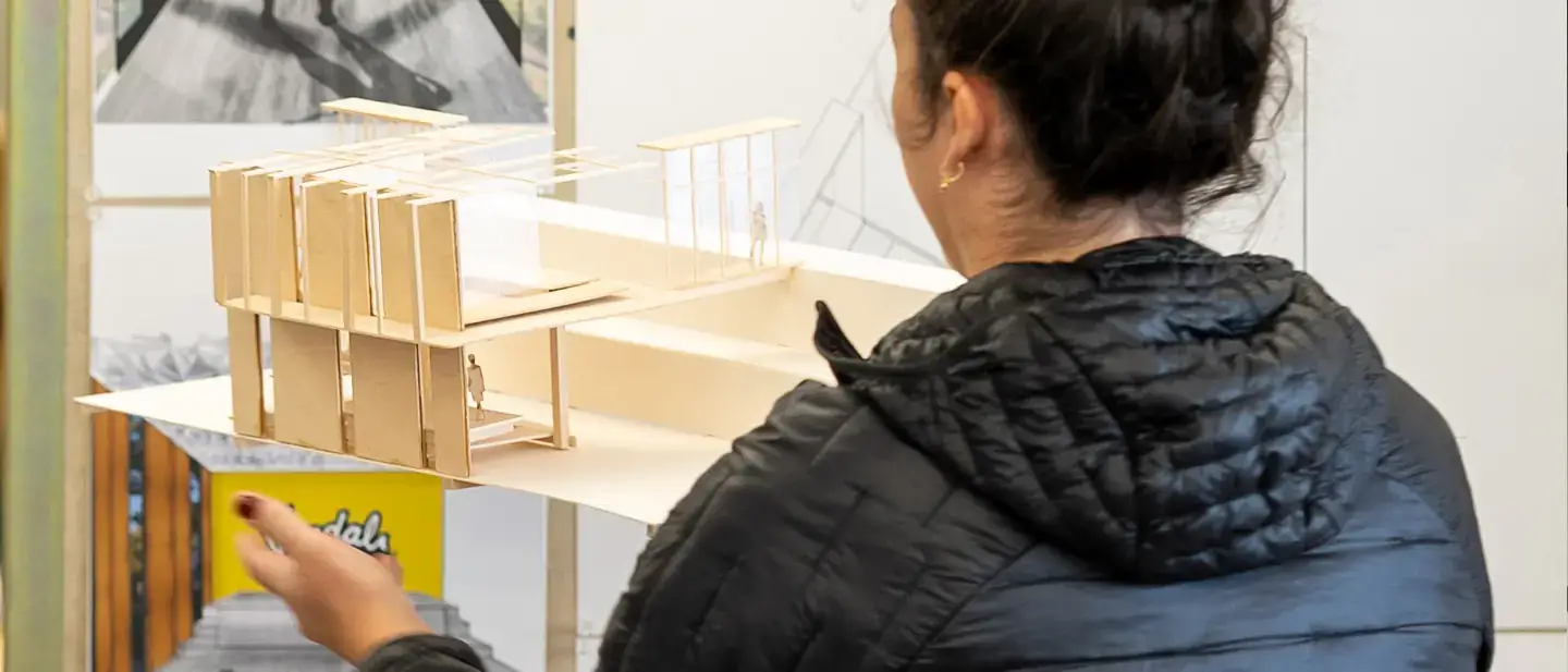 A person examines a detailed architectural scale model in a creative workspace.