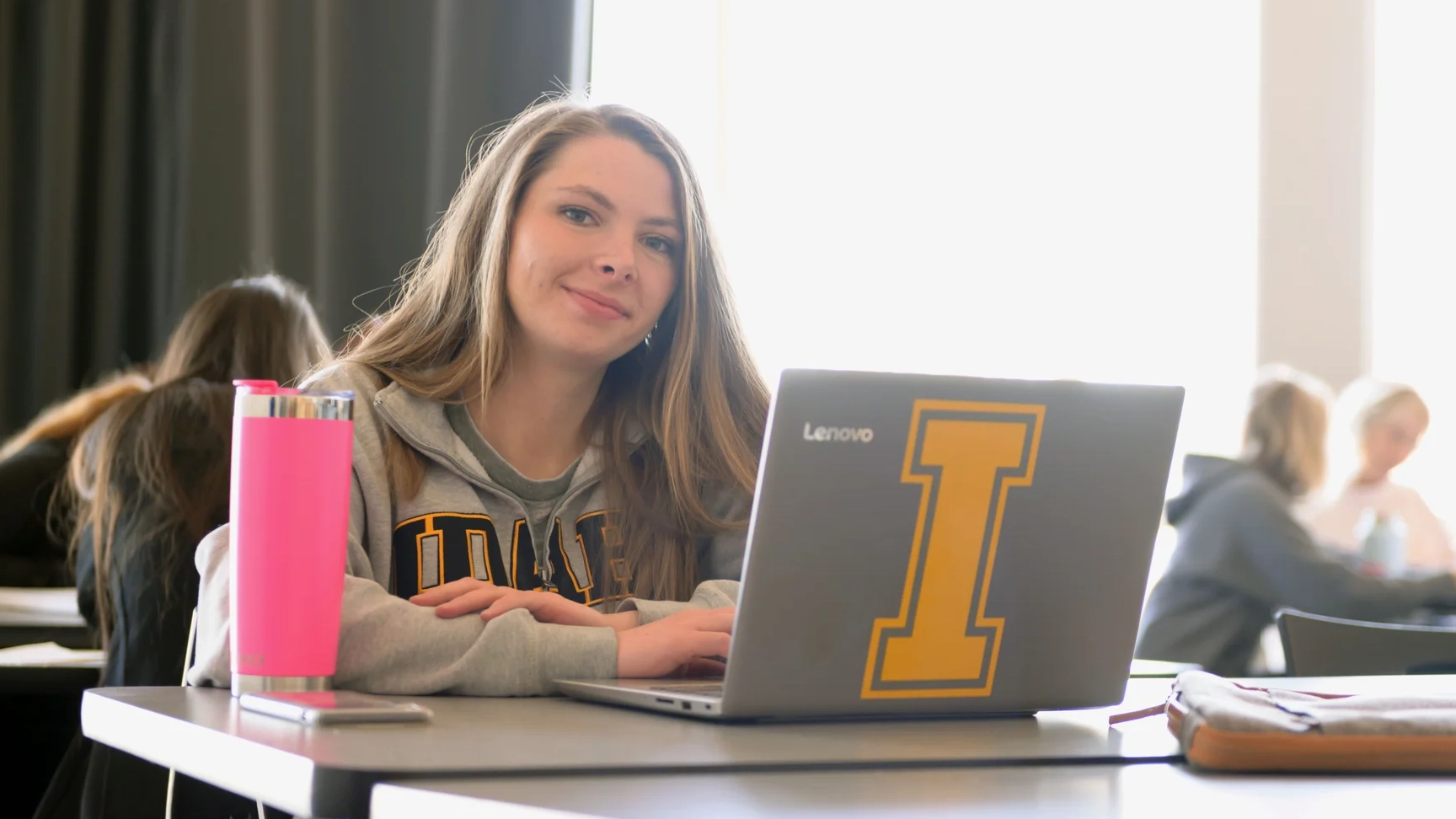 International student sitting at a table behind a laptop looking at the camera. 