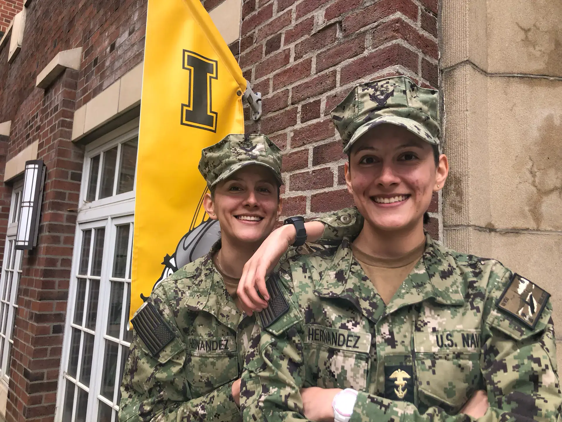 Two women in uniform stand in front of the Alumni Relations office.